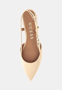 Beige kiilakärkinen slingback-kengät, joissa on metallinen solki nilkkahihnassa ja sileä, kiiltävä pinta.