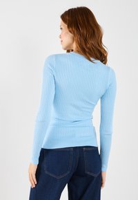 Lichtblauwe ribbelende langemouwen top met een v-hals en een aansluitend ontwerp, gecombineerd met donkere denim jeans, die de gladde textuur van de stof laat zien.