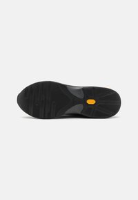 Semelle en caoutchouc noir avec des motifs texturés, arborant un logo Vibram jaune bien en vue, conçue pour l'adhérence et la durabilité.
