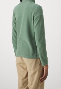 Fleece pullover in zachte groene kleur, met een hoge kraag en lange mouwen. De gladde textuur past perfect bij de ontspannen pasvorm en casual stijl.