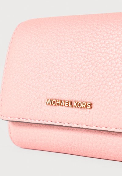 Portefeuille en cuir rose doux texturé avec le nom de la marque "Michael Kors" en or centré sur le rabat avant, sur un fond clair uni.