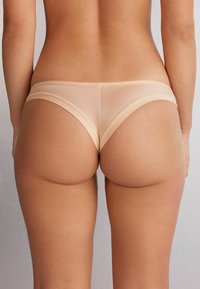 Licht beige naadloze slipjes van een rekbaar, glad materiaal. Laag uitgesneden ontwerp met minimale bedekking en platte elastische banden langs de randen.