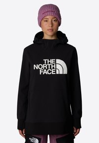 Svart pulloverjacka med en stor vit logotyp på framsidan, med huva och elastiska muddar, matchad med en rosa ribbad stickad mössa.