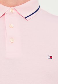 Ανοιχτό ροζ πόλο πουκάμισο με υφή στο ύφασμα, διαθέτει γιακά με άσπρες και ναυτικές ρίγες και τρία κουμπιά στο λαιμό. Μικρό λογότυπο στο στήθος.