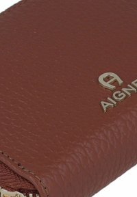 Brown textured leather wallet with a gold metal logo. Features a zip closure and a smooth, slightly shiny finish.