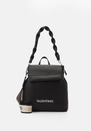 Sac à dos en cuir noir avec une forme structurée, poignée matelassée, rabat repliable et un logo argenté à l'avant ; bandoulière accentuée en beige et noir.
