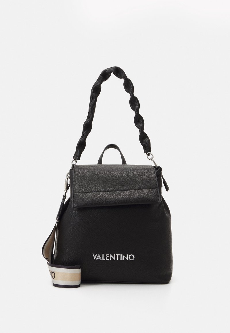 Sac à dos en cuir noir avec une forme structurée, poignée matelassée, rabat repliable et un logo argenté à l'avant ; bandoulière accentuée en beige et noir.