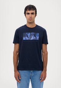 T-shirt in cotone blu navy con stampa grafica in toni di blu e il testo "AX" e "ARMANI EXCHANGE". Design a maniche corte e collo rotondo.