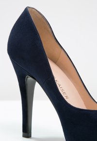 Escarpin en daim bleu marine à talon haut avec un bout pointu et un talon aiguille élégant. L'intérieur présente une doublure claire, mettant en avant le branding.