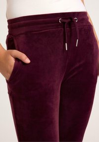 Burgundy velour joggers featuring a drawstring waistband, two side pockets, and a soft, smooth texture.