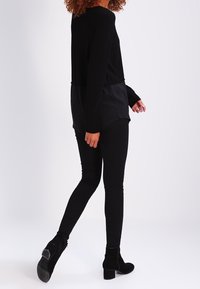 Svart långärmad topp med satinbak, kombinerad med svarta åtsittande leggings och ankelboots. Svala texturer och slank siluett.