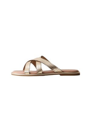 Flad sandal med beige krydsede læderremme med bølgede kanter og syningsdetaljer, vist fra siden på en hvid baggrund.