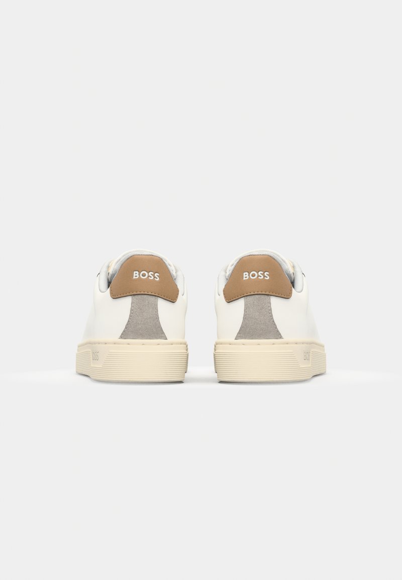 Baskets en cuir blanc avec un accent de talon en daim beige, une semelle en caoutchouc texturée et un logo embossé sur le talon.