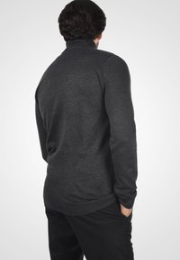 Suéter de color gris oscuro con cuello alto, mangas largas y dobladillo acanalado. Textura suave con una forma ajustada.