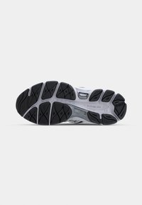 Semelle en caoutchouc noir et gris crantée d’une chaussure de course vue par dessous, mettant en avant les motifs d’adhérence et les rainures de flexibilité.