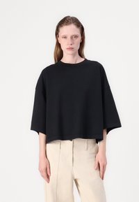 Μαύρο oversized κοντομάνικο μπλουζάκι με φαρδύ λαιμό και μαλακή υφή, σε συνδυασμό με ανοιχτό μπεζ παντελόνι ψηλόμεσο.