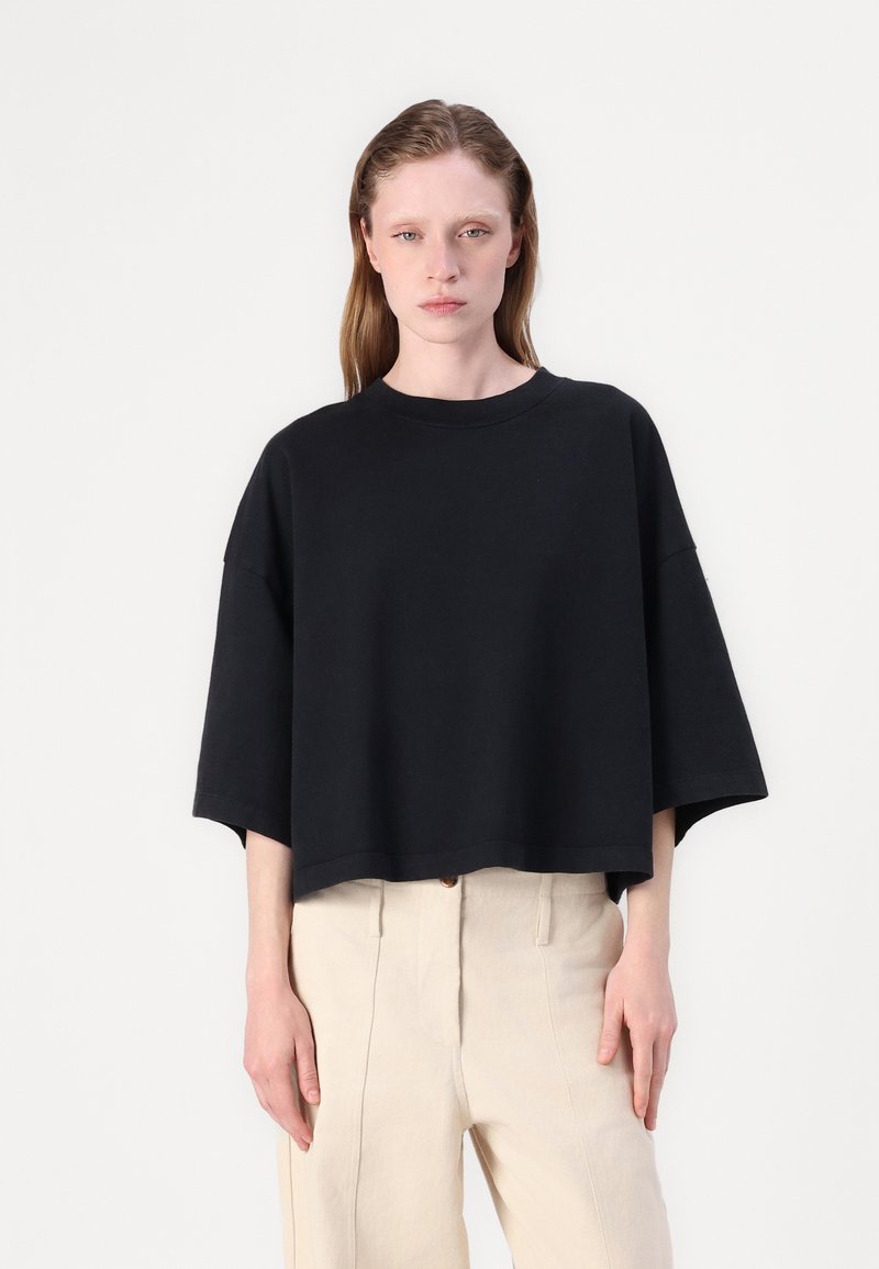 Μαύρο oversized κοντομάνικο μπλουζάκι με φαρδύ λαιμό και μαλακή υφή, σε συνδυασμό με ανοιχτό μπεζ παντελόνι ψηλόμεσο.