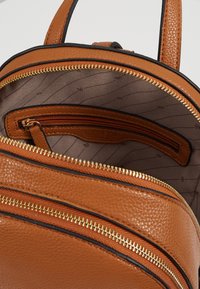 Sac à dos en cuir texturé brun avec des zippers dorés et une petite poche intérieure zippée sur une doublure en tissu à motifs légers.