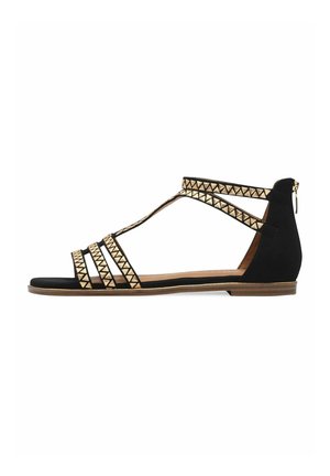 Sandali piatti neri con accenti triangolari dorati, caratterizzati da un design con T-strap, punta aperta e chiusura con cerniera sul tallone.
