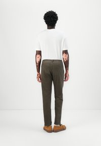 Vit t-shirt och olivgröna byxor med elastisk midja, kombinerat med bruna skor. Slät textur och avslappnad passform, sedd från ryggen.