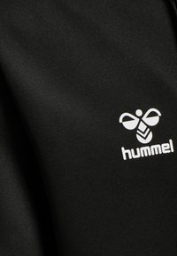 Tejido atlético negro con una textura suave que presenta un logo blanco de Hummel. El diseño es sencillo, sin patrones ni acentos adicionales.
