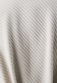 Bílá látka s vyvýšenou diagonální pruhovanou texturou, která vytváří jemný, vlnitý vzor.