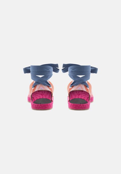 Ζευγάρι πολύχρωμα πλατφόρμες με ροζ σόλες, πορτοκαλί λουράκια και ναυτικού μπλε δεσίματα στον αστράγαλο με σταυρωτό σχέδιο, εμφανιζόμενα από πίσω.