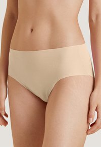 Beige katoenen stretch slips met een hoge taille, een gladde textuur en naadloze randen, ontworpen voor comfort en pasvorm. Geen zichtbare patronen of bevestigingen.