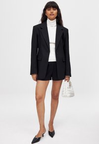 Juodas didelis švarkas virš balto golfuko, derinamas su juodomis šortais ir smailiais juodais aukštakulniais. Išvaizdą užbaigia nedidelė balta pintinė rankinė.