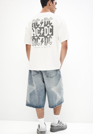 White cotton T-shirt with black AC/DC graphic on back; paired with light blue denim shorts featuring star patterns. Gray sneakers and white socks.