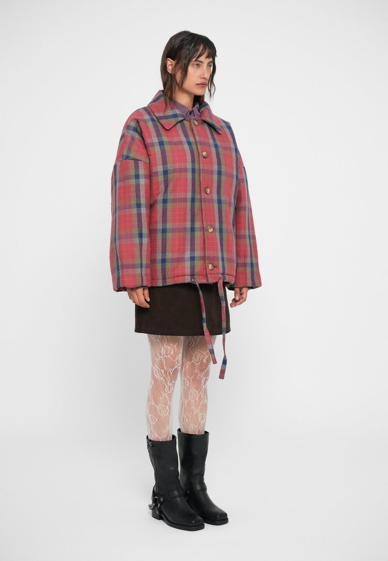 Plaid shirt jacket in red, blue, and green with oversized fit, button closure, and large collar. Worn over a brown skirt and patterned tights.