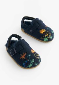 Chaussons en feutre bleu marine avec une doublure intérieure douce, ornés de motifs colorés de dinosaures et de plantes brodés, et une sangle à boucle pour un maintien sûr.