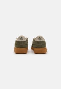 Grüne Wildleder-Sneaker mit beigen Lederelementen und einer braunen Gummisohle. Mit eingeprägtem Logo an der Ferse. Niedriges Design.