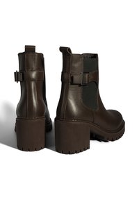 Bruine leren enkelboots met elastische zijpanelen, een robuuste blokhak en gespaccents. Geverfde rubberen zool voor grip.