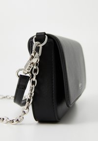 Zwarte leren crossbodytas met zilveren kettingriem en sluiting, zijdelings weergegeven op een witte achtergrond.