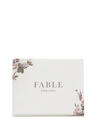Balta kaste ar tekstu „FABLE ENGLAND“, dekorēta ar rozā un zaļiem ziedu motīviem augšējā kreisajā un apakšējā labajā stūrī.