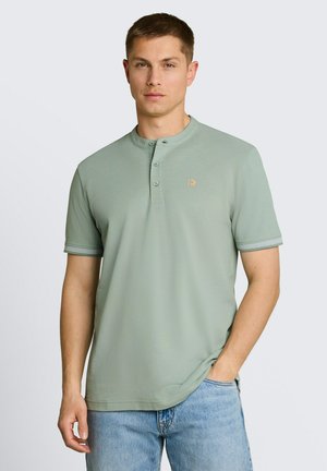 Uomo che indossa una maglietta Henley verde chiaro a maniche corte con tre bottoni e un piccolo logo arancione, abbinata a jeans azzurri.