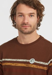 Brown sweatshirt with white, yellow, and red horizontal stripes. Features a round logo patch on the chest. Soft fabric, crew neckline.