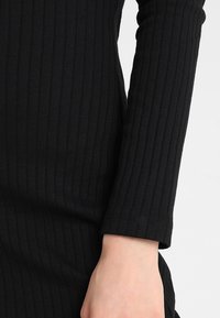 Czarny prążkowany longsleeve z dopasowanym krojem i subtelną teksturą. Zawiera dopasowany mankiet w okolicy nadgarstka.