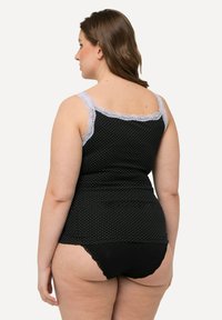 Camiseta de tirantes negra con lunares y bordes de encaje, diseño ajustado y textura suave, combinada con ropa interior negra con detalles de encaje.