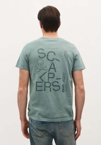Grøn bomulds T-shirt med store sorte grafik og tekst på ryggen, herunder et skelet og tværknogler, med en afslappet pasform.