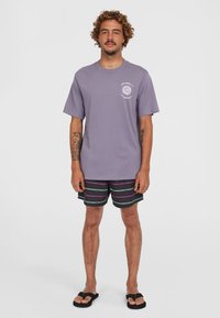 Licht paarse T-shirt met korte mouwen en een witte zonafbeelding op de borst, gecombineerd met gestreepte zwarte shorts met groene, paarse en roze accenten.