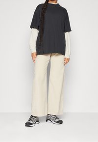 Zwarte oversized t-shirt gelaagd over een lichtbeige langemouwen top, gecombineerd met brede beige broek en grijze sportschoenen.