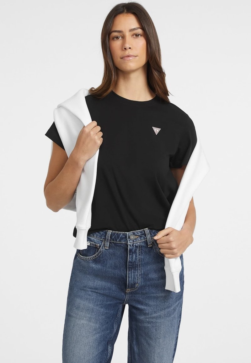 Black cotton t-shirt with short sleeves and a small triangle logo on the chest, paired with high-waisted blue denim jeans and a white sweatshirt draped over the shoulders.