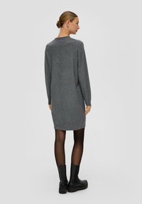 Šedé pletené šaty s dlouhými rukávy, volným střihem a švy. Nosené s černými koženými botami na podpatku a černými punčochami. Minimalistický design.