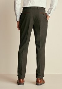 Pantalones de color gris oscuro con un corte ajustado, que cuentan con dos bolsillos traseros con detalles en marrón y dobladillos acampanados. Combinados con zapatos marrones.