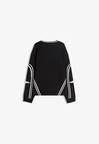 Svart tröja med vita diagonala ränder och chevrondesign. Stickad textur, sänkt axelsöm och ribbade ärmslut och nederkant.