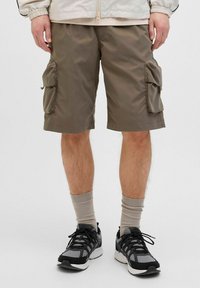 Olijfgroene cargoshorts van stof met twee zijzakken, rechte pasvorm, knie-lengte. Gecombineerd met grijze en zwarte sportschoenen en geribbelde sokken.
