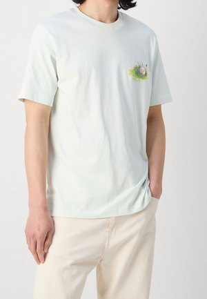 Hellmintgrünes Baumwoll-T-Shirt mit kurzen Ärmeln und rundem Halsausschnitt. Auf der linken Brust befindet sich ein kleines, buntes Grafikdesign.