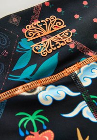 Daudzkrāsains audums ar ziedu un viļņu rakstiem; uz tumša fona atrodas oranžs dekoratīvs akcents. Redzama kontrastūšņošana.